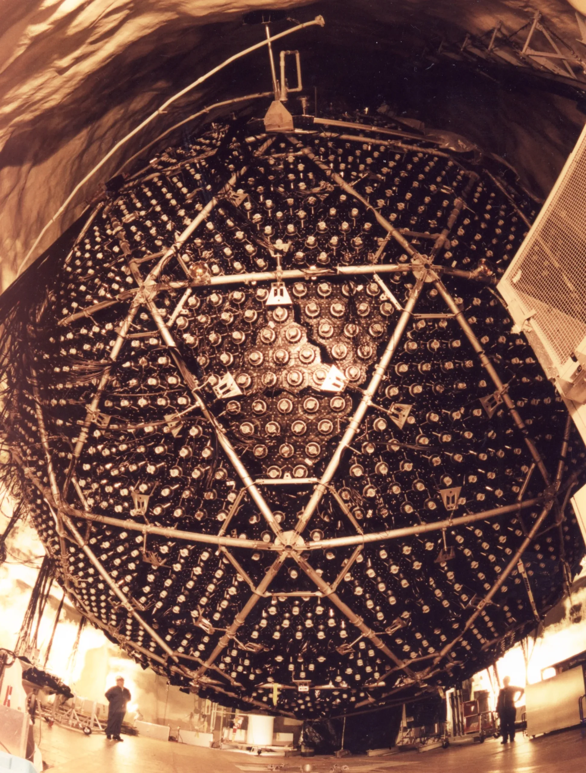 A very large black sphere dotted with silver instruments suspended inside a cavern.