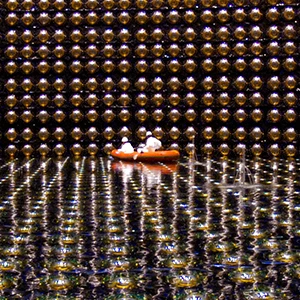 A large cavern lined with reflective spheres and partially filled with water. Two people in white protective gear float in an orange raft in the distance.