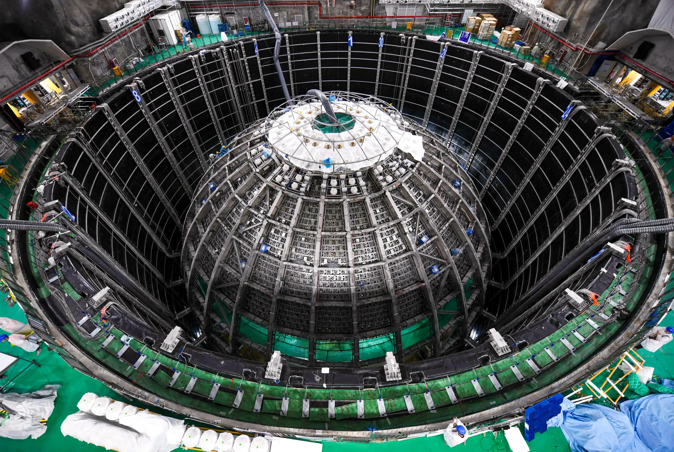 Aerial view looking down into a large cylindrical detector under construction, showing a dome-shaped inner structure surrounded by scaffolding and detector components.