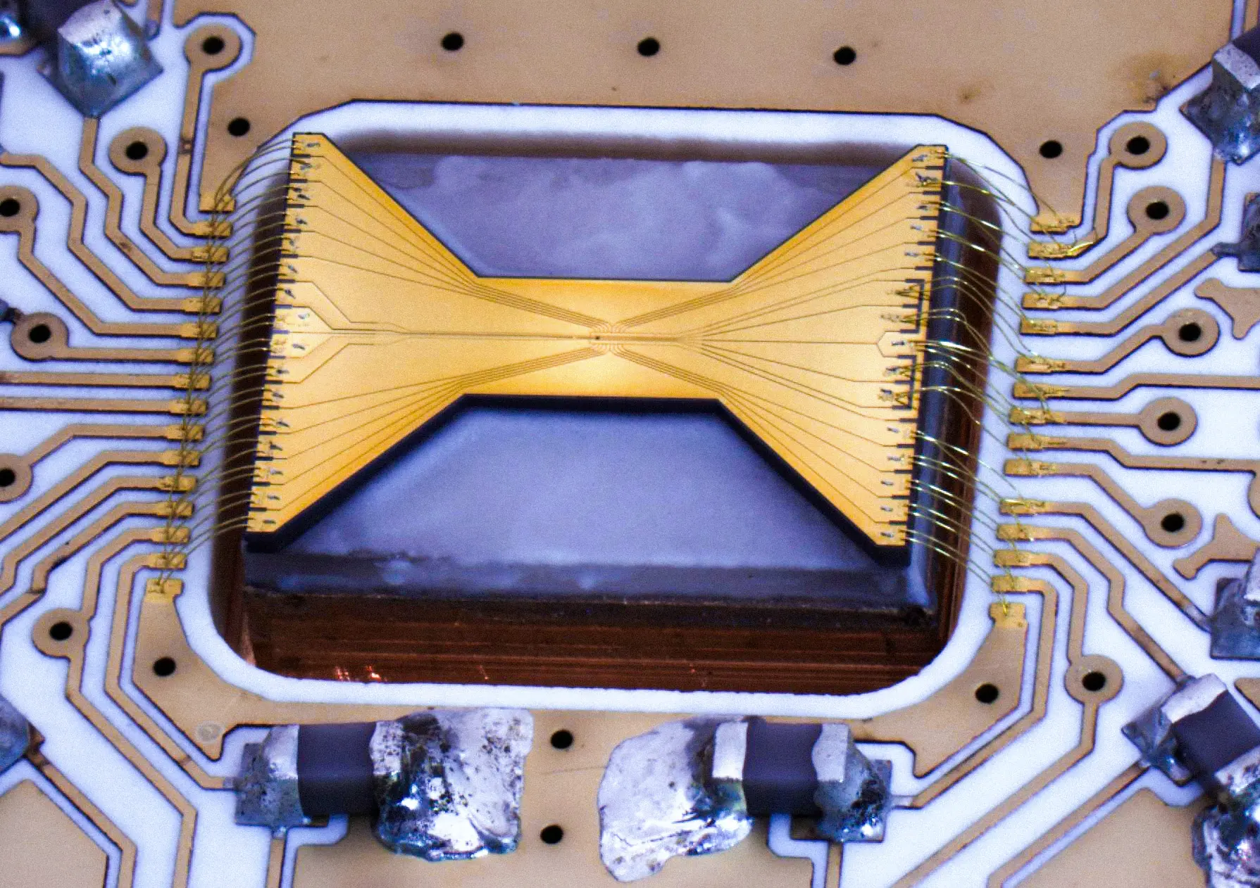 View of a bowtie-shaped ion trap chip patterned with electrodes and mounted on a circuit board.
