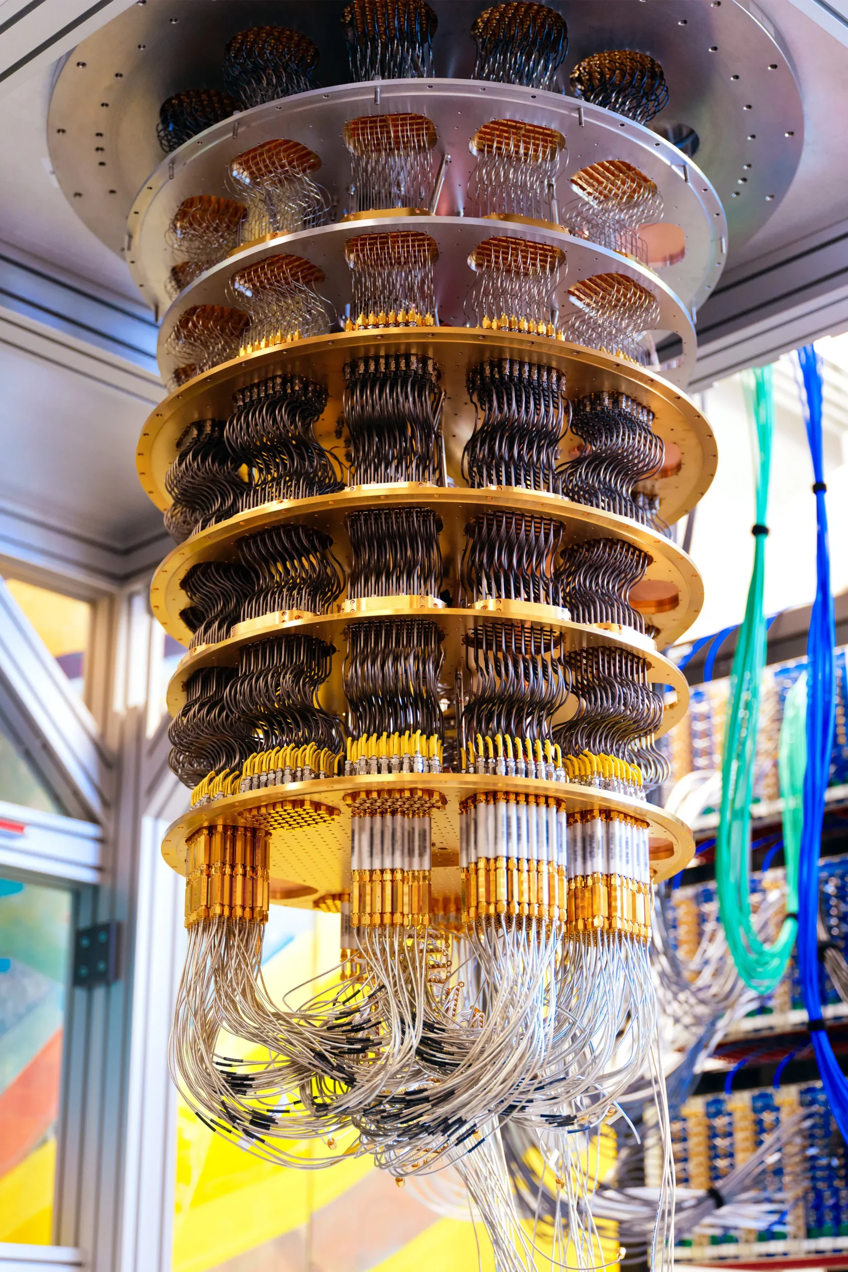 A larger chandelier-like dilution refrigerator with several gold-colored cooling plates, densely wired with hundreds of cables.