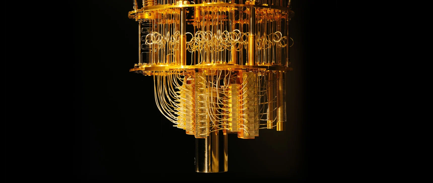 Close-up view of a chandelier-like dilution refrigerator used in quantum computing, with many gold-colored wires hanging between levels of gold plates.