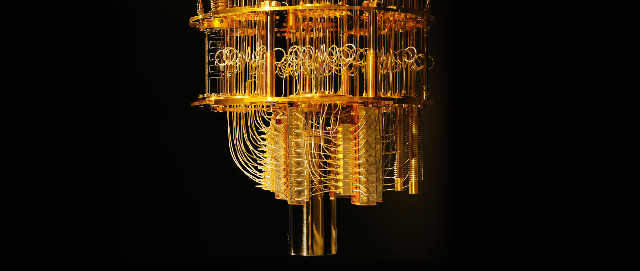 Close-up view of a chandelier-like dilution refrigerator used in quantum computing, with many gold-colored wires hanging between levels of gold plates.