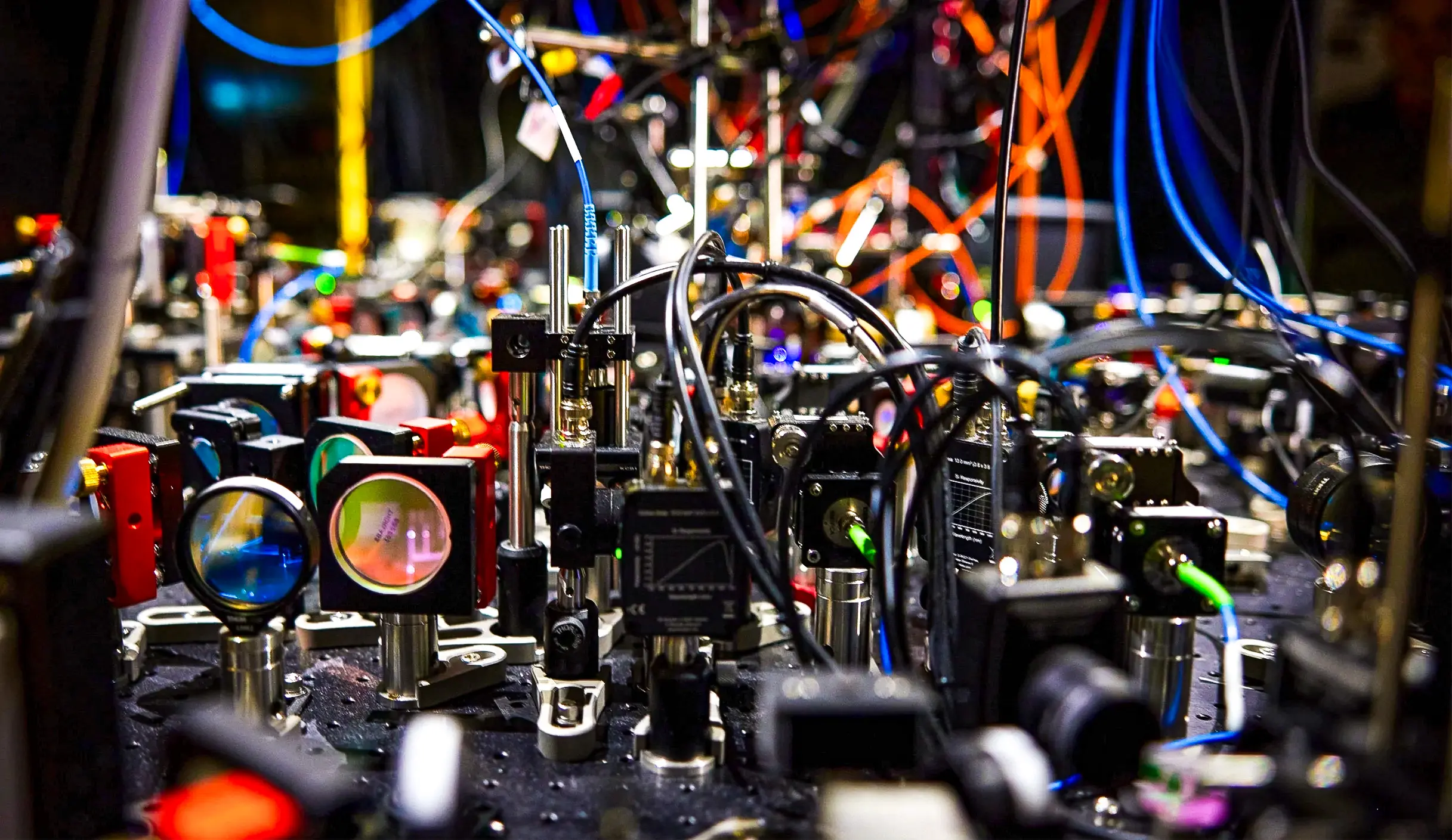 An optical table setup in a laboratory, with mirrors, lenses, optical fibers, and photodetectors visible.